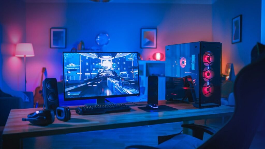 Modern RGB-lit gaming setup featuring a desktop PC, large monitor, speakers, keyboard, and gaming hardwere and accessories in a blue and pink LED room.